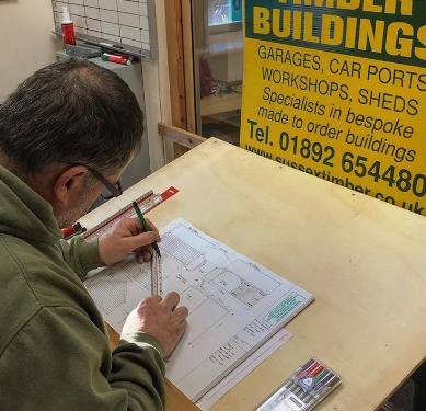 A photo of a man drawing a plan for a timber building