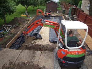 A photo of a digger in a garden putting soil into a raised bed