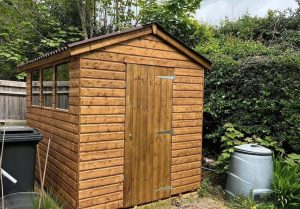 A photo of a potting shed in a garden next to a compost bin